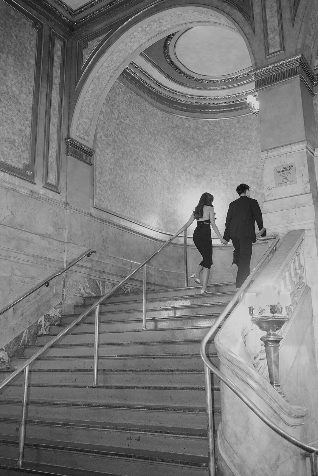 Bryan and Sheryl walking upstairs hand in hand, in black and white